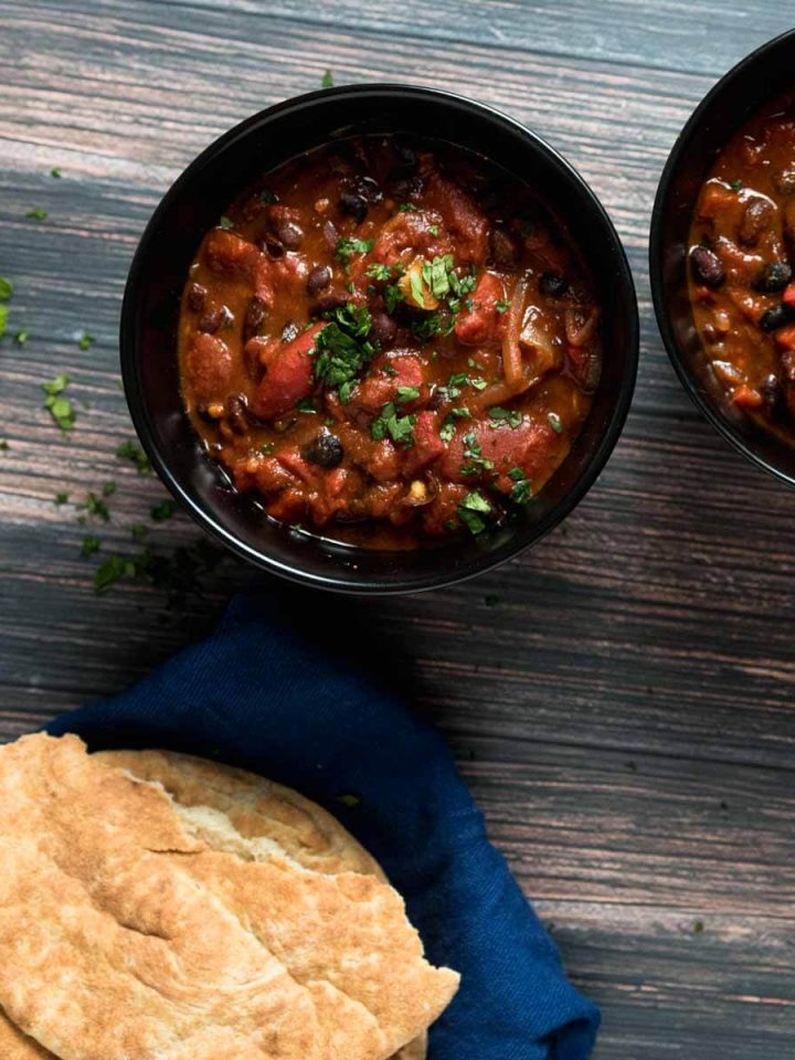 two bowls of black bean and chipotle stew served ith pita bread