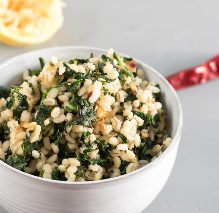 barley with lemon and kale in a white bowl, lemon and chili pepper in background