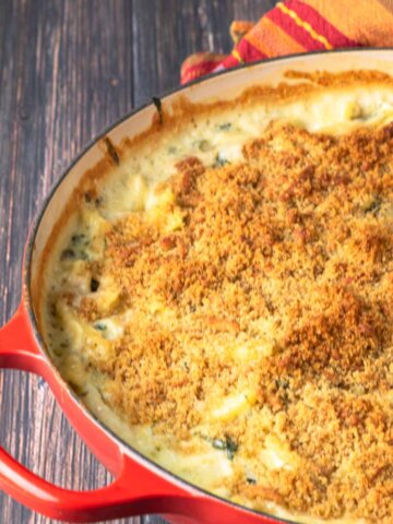 spinach mac and cheese with crispy bread crumb topping in a red casserole dish