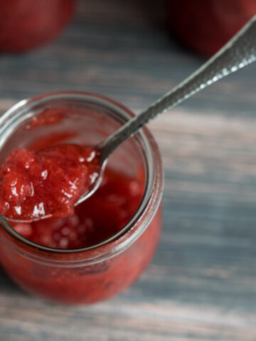 open jar of honey strawberry jam with a spoon in it