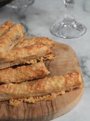 Crispy, homemade cheese straws on a wooden serving board, wine glass in background, marble surface, recipe for entertaining at home, New Year's Eve, appetizers